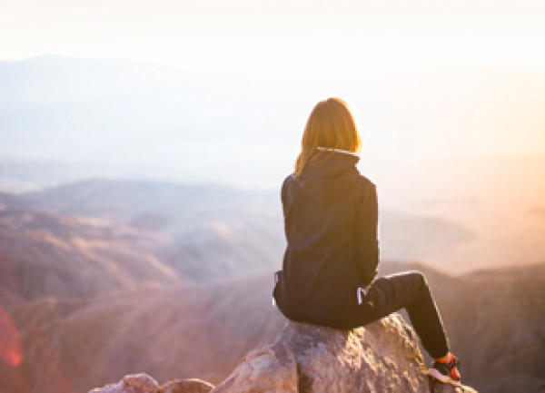 A woman sitting on a rock looking out over mountains